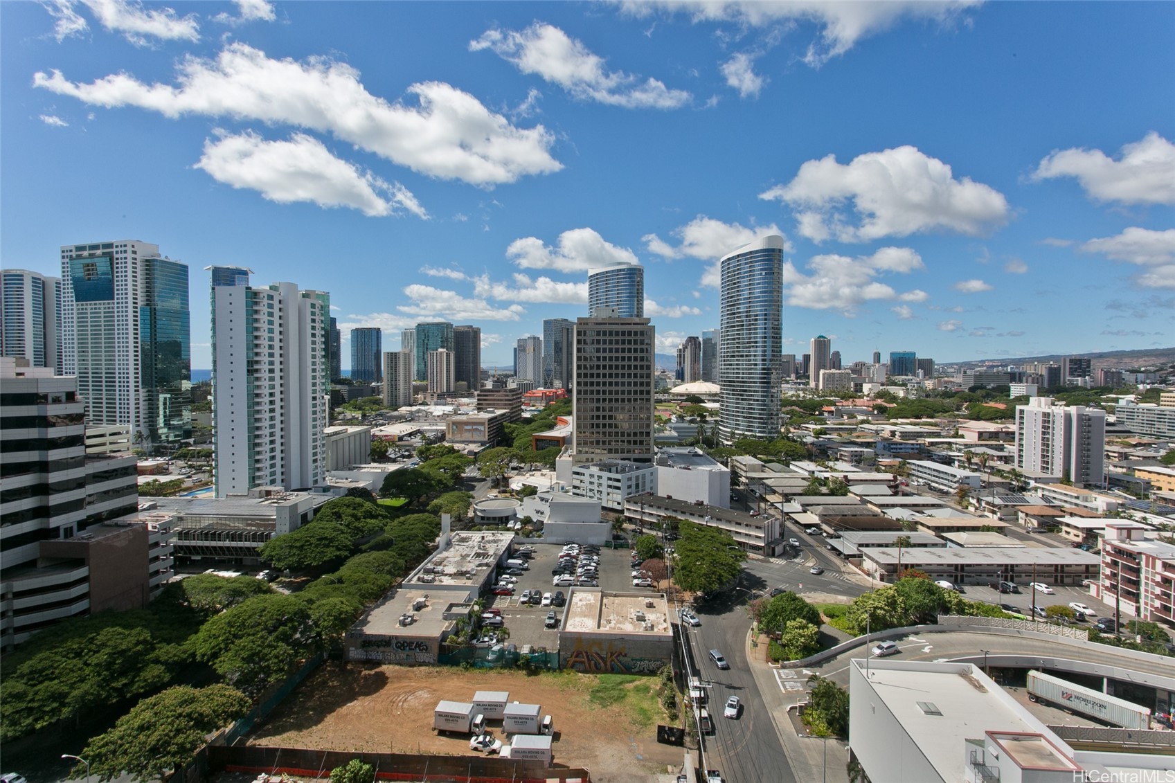 Honolulu city skyline viewed from above, with high-rise towers beneath a bright, cloud-filled sky.