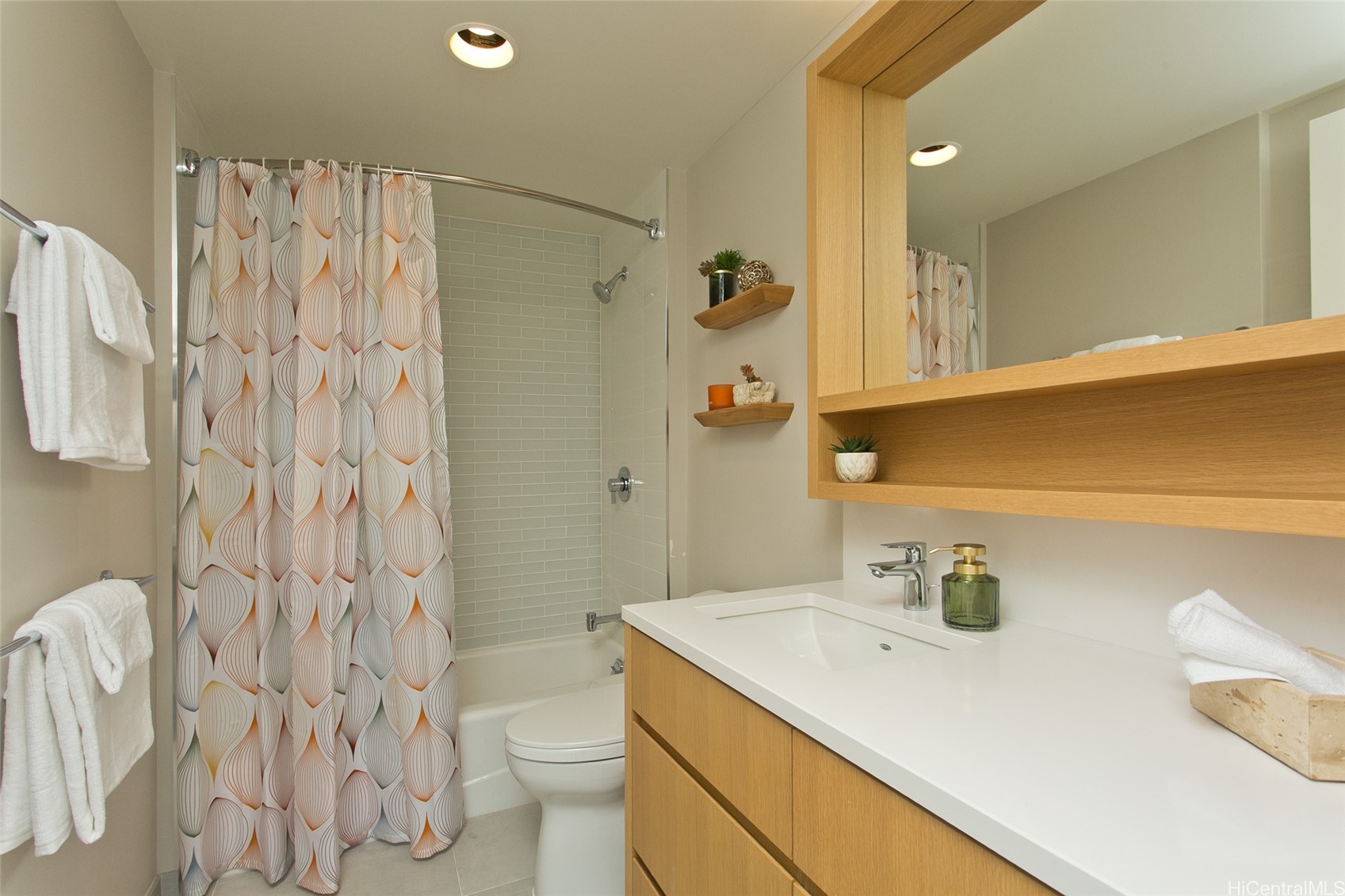 Bathroom with a patterned shower curtain, pale subway tile, and a light wood vanity.