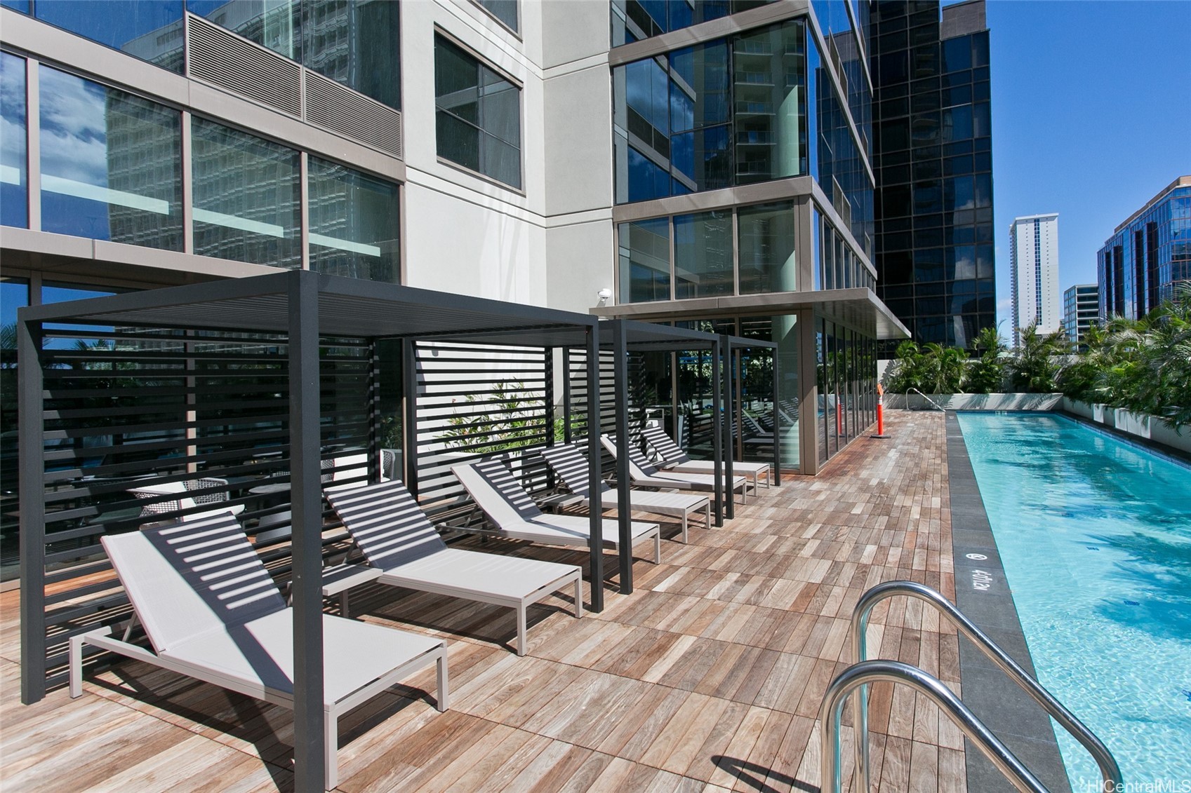 High-rise pool deck with shaded cabanas, white lounge chairs, and surrounding city buildings.