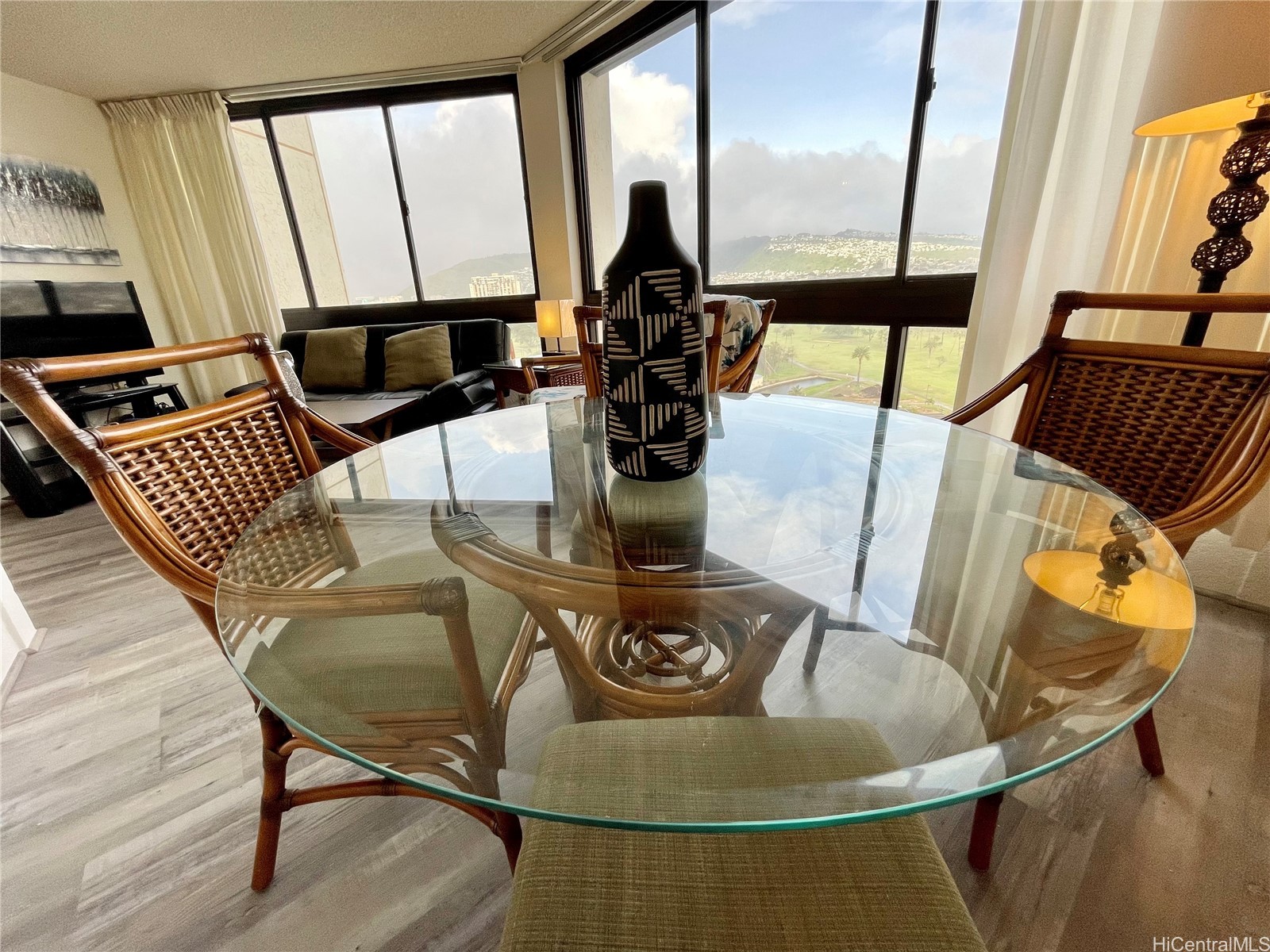 Condo dining area with a glass table and wicker chairs overlooking a golf course and hills.