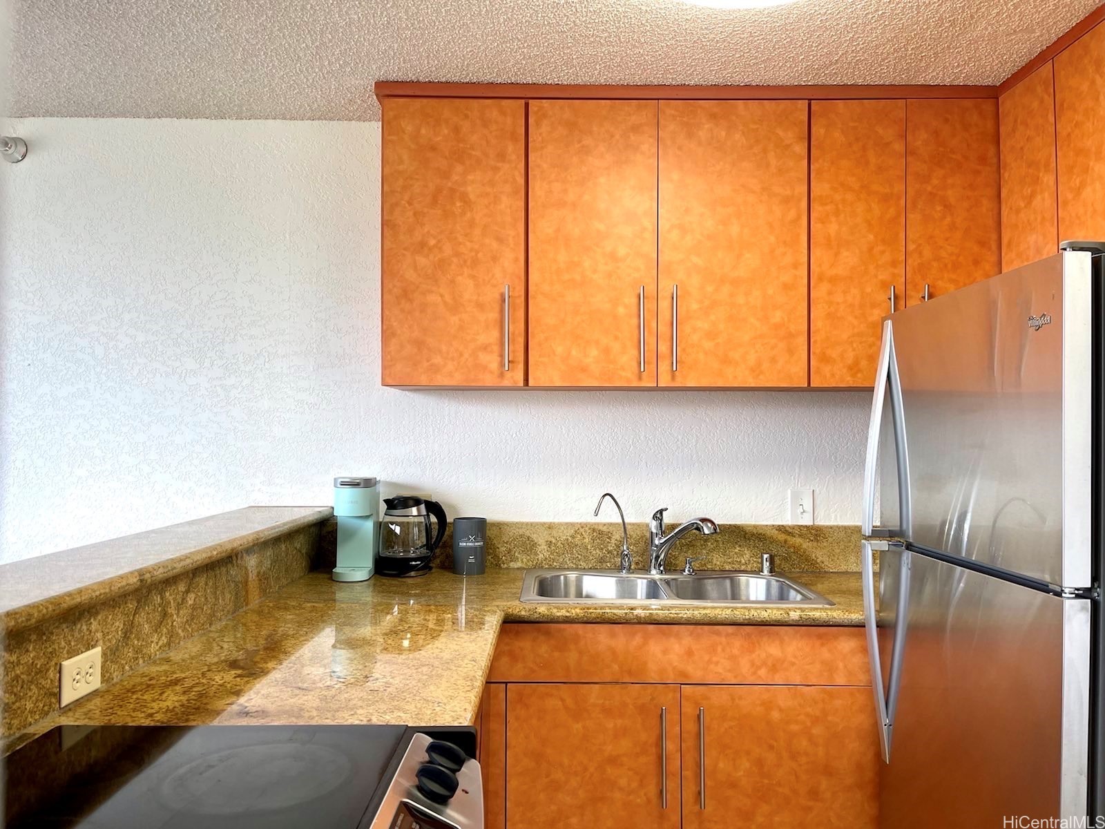 Kitchen with orange-toned cabinets, mottled brown counters, a double sink, and stainless-steel appliances.