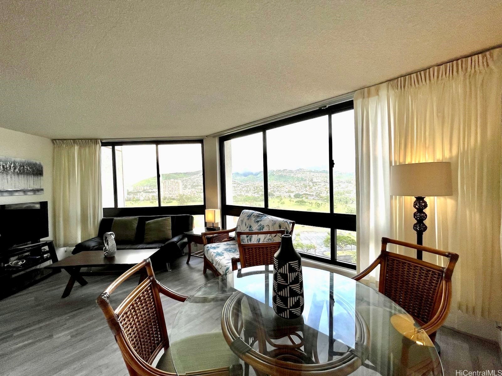 Living and dining area with floor-to-ceiling windows overlooking a golf course and hills.