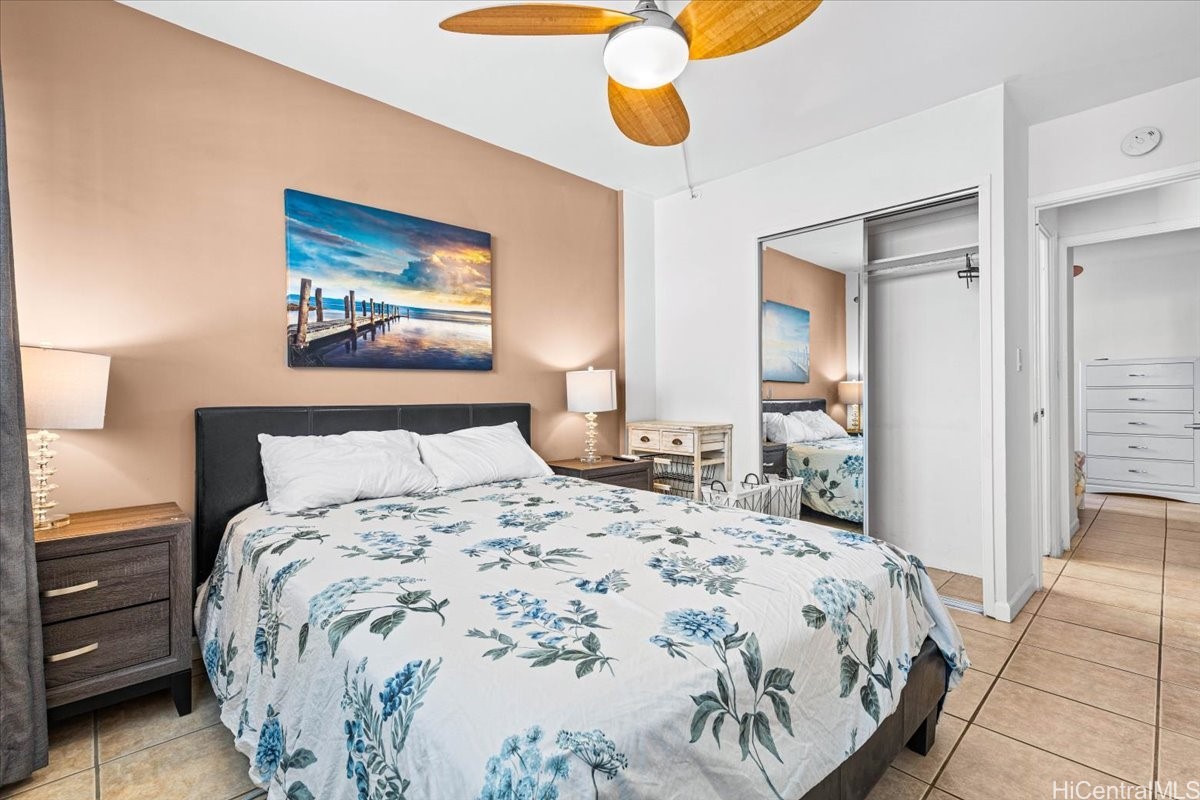Furnished bedroom with a floral bedspread, mirrored closet doors, and a wooden-blade ceiling fan.