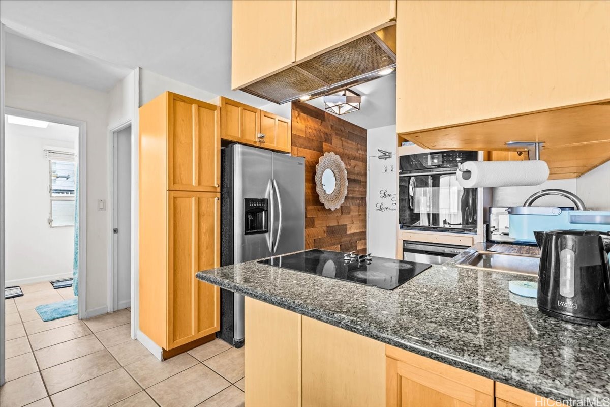 Kitchen with granite peninsula, black cooktop, honey-colored cabinets, and stainless steel appliances.