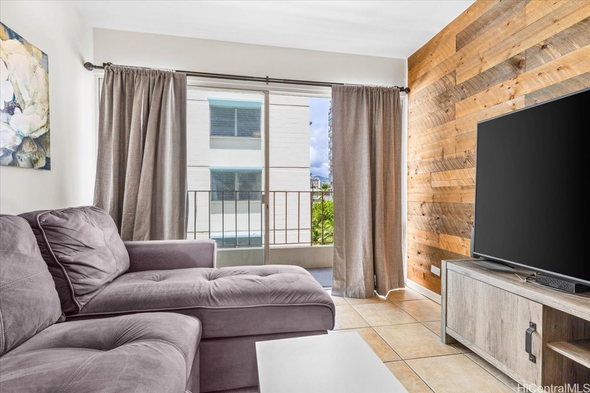 Living room with a gray sectional, wood-plank accent wall, and sliding glass door to a balcony.