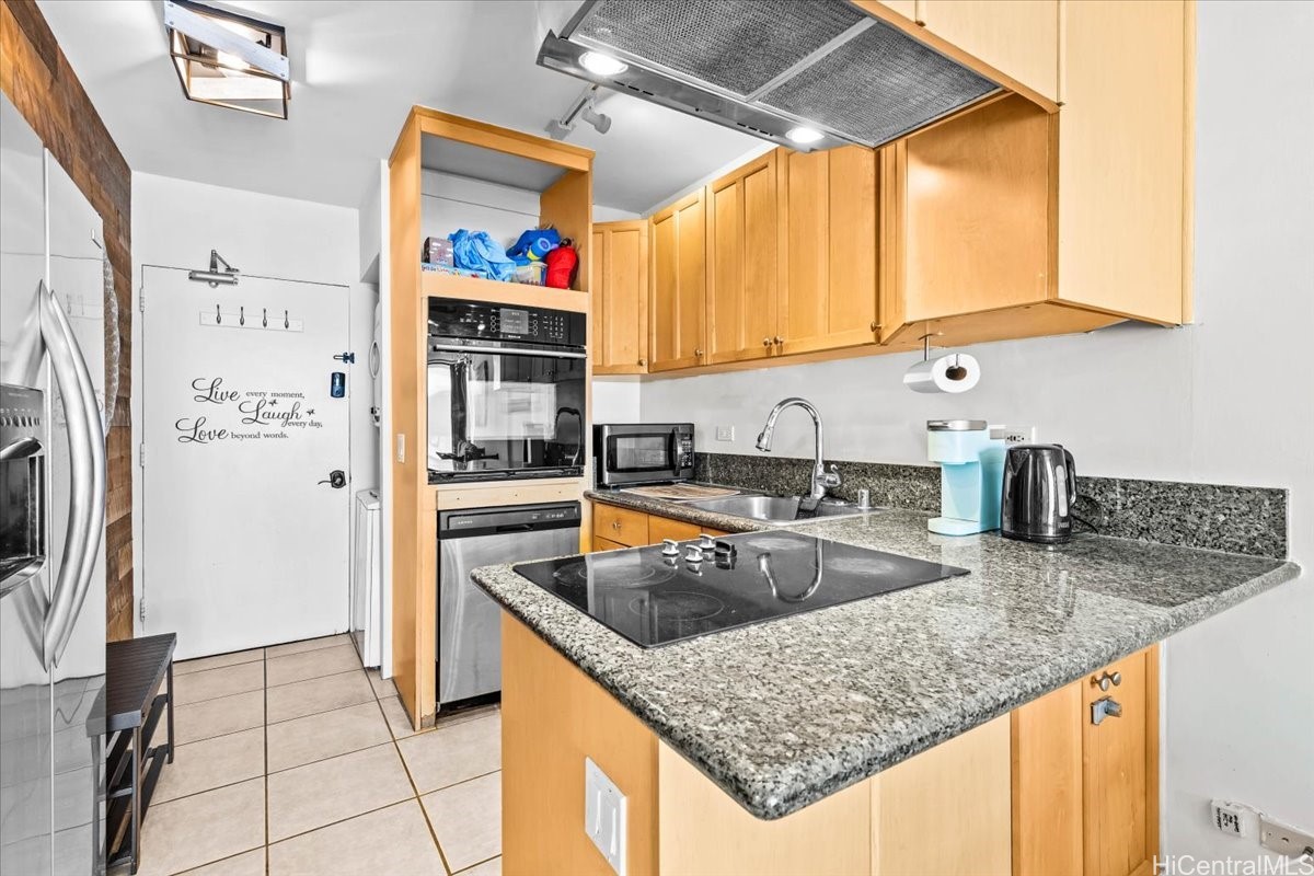 Kitchen with honey-colored cabinets, granite counters, a breakfast bar cooktop, and stainless steel appliances.