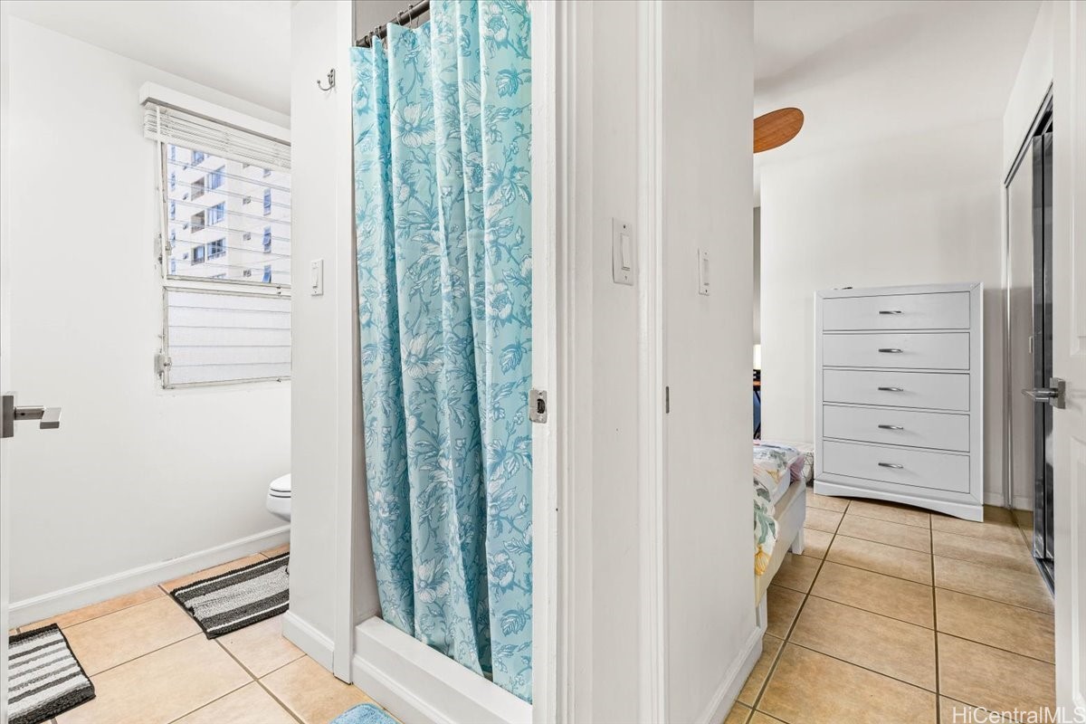 Bathroom with a blue floral shower curtain opening onto a bedroom with a white dresser.