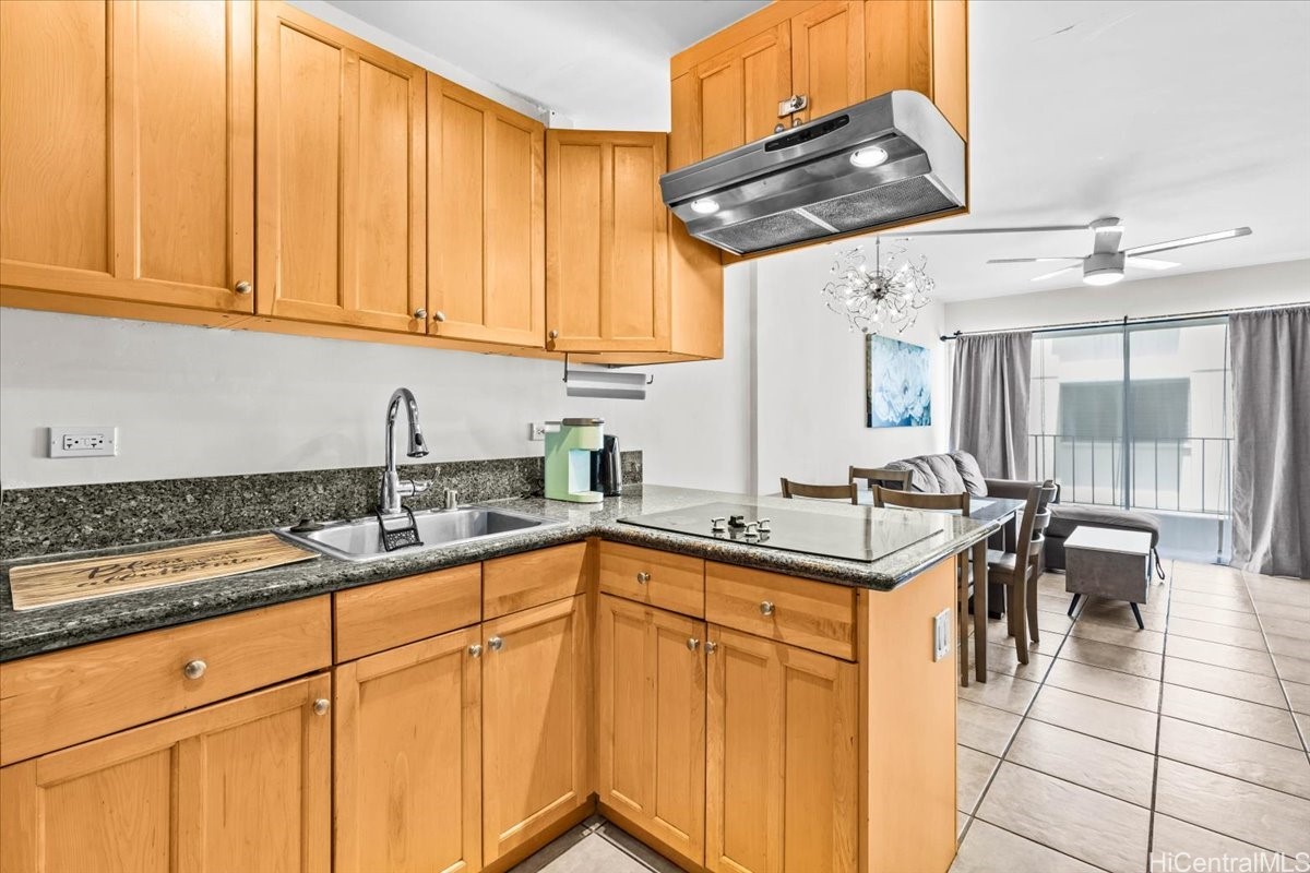 Condo kitchen with honey-colored cabinets and granite counters opening to a furnished living area.