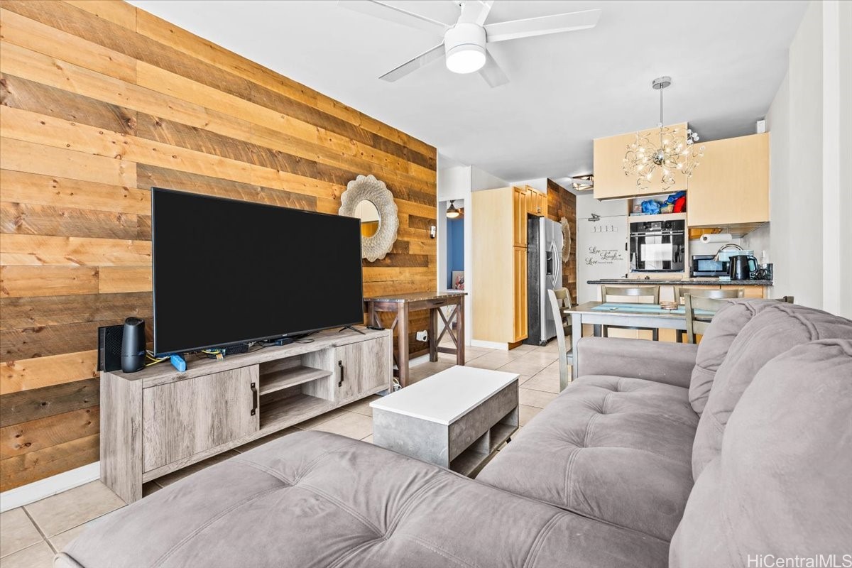 Living room with a gray sectional, rustic wood accent wall, and open kitchen.