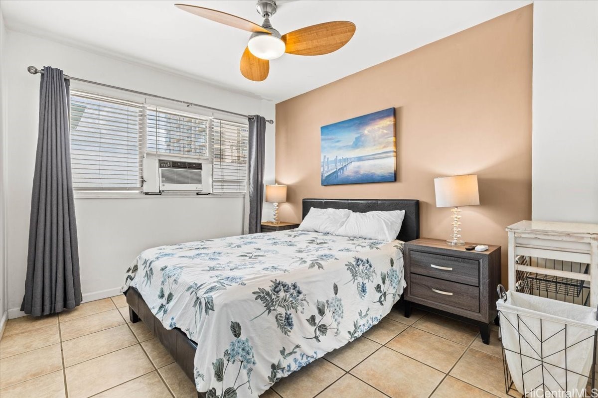 Bedroom with a floral-covered bed, peach accent wall, and window air conditioner.