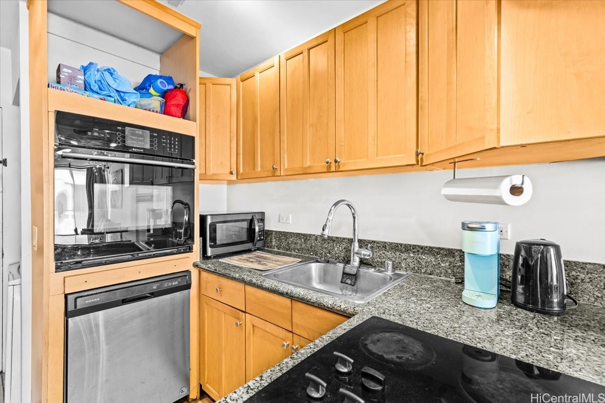 Compact kitchen with honey-colored cabinets, granite counters, and built-in stainless appliances.