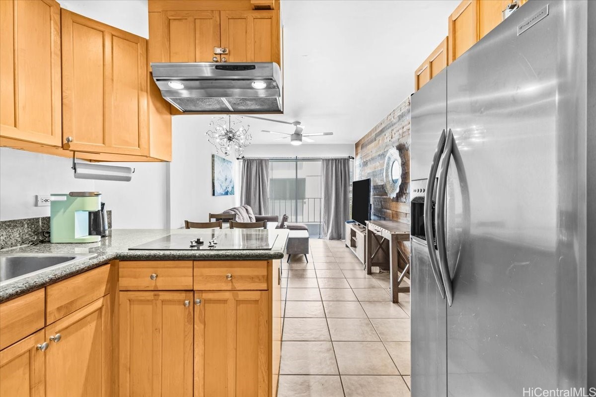 Condo kitchen with honey-colored cabinets and granite counters opening into a tiled living area.