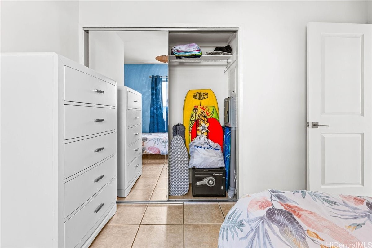 Bedroom with mirrored closet doors, white dressers, tiled floor, and a surfboard stored in the closet.