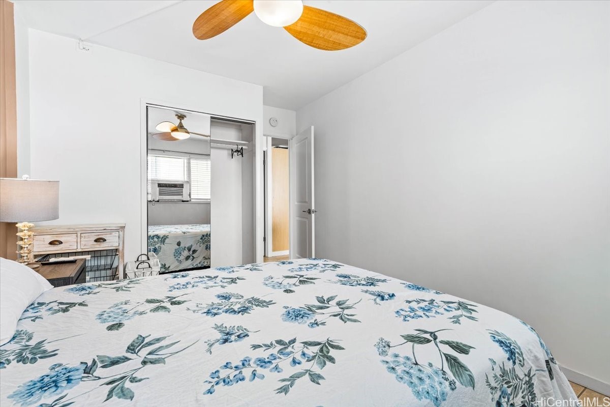 Bedroom with blue floral bedding, a mirrored closet, and a wooden-blade ceiling fan.