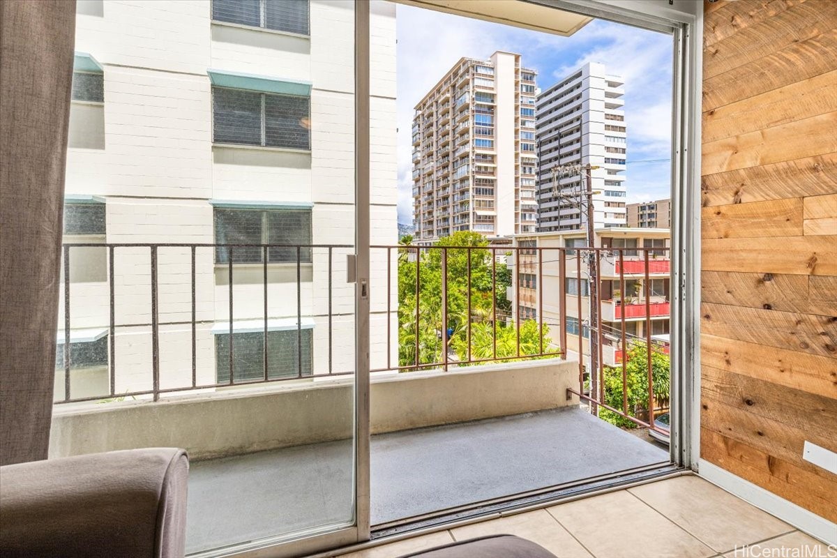 Condominium balcony overlooking nearby high-rises and tropical greenery, framed by sliding glass doors.