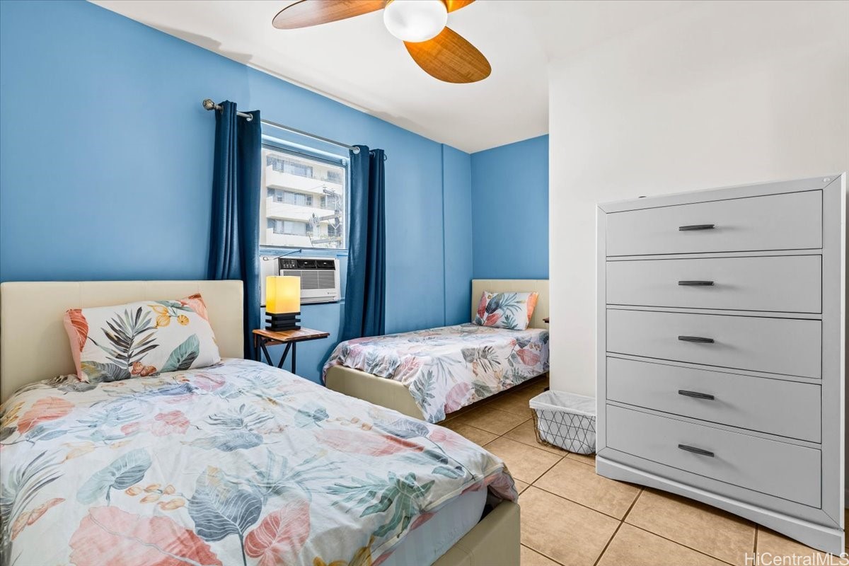 Bedroom with two tropical floral twin beds, blue walls, and a window air conditioner.