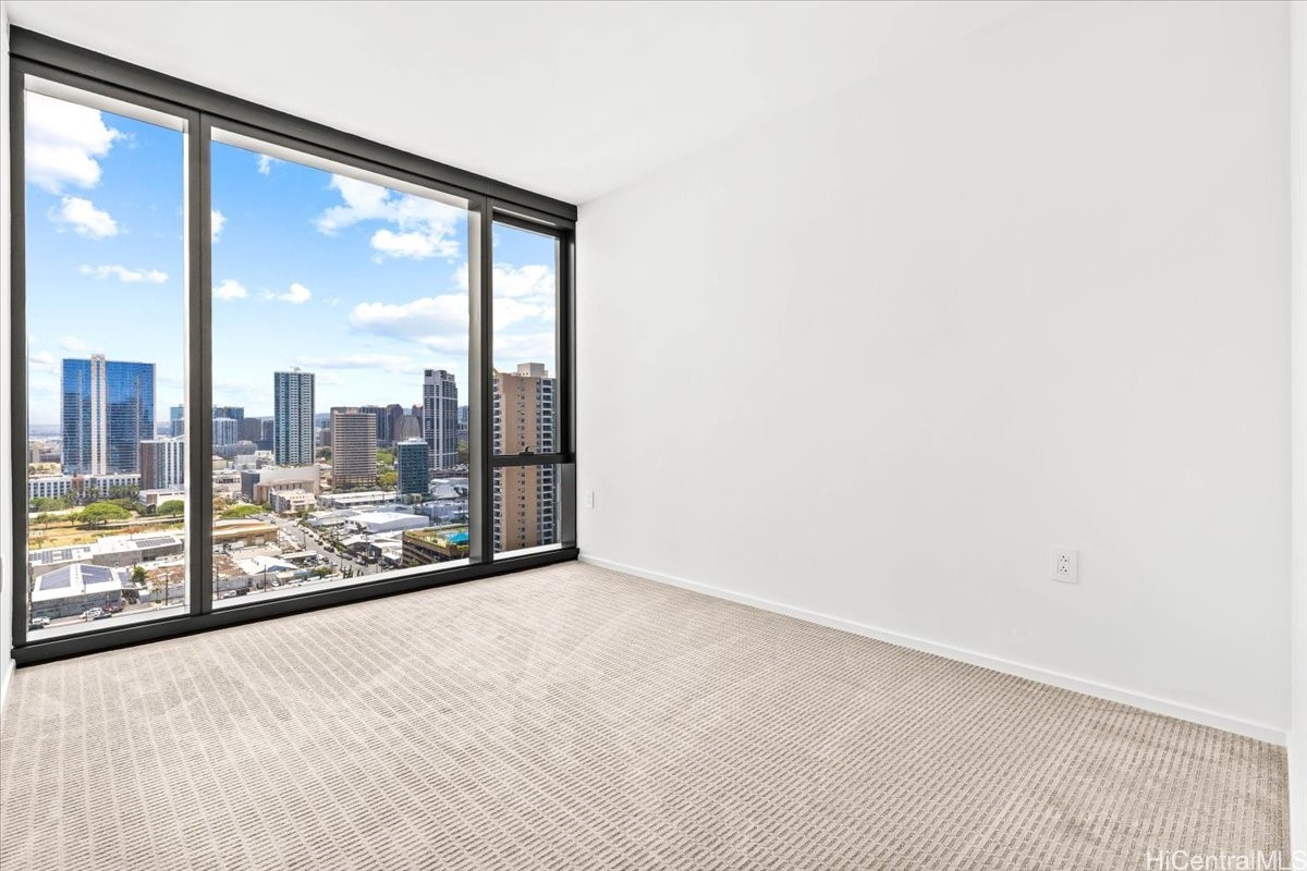 Empty carpeted room with floor-to-ceiling windows overlooking Honolulu's downtown skyline.