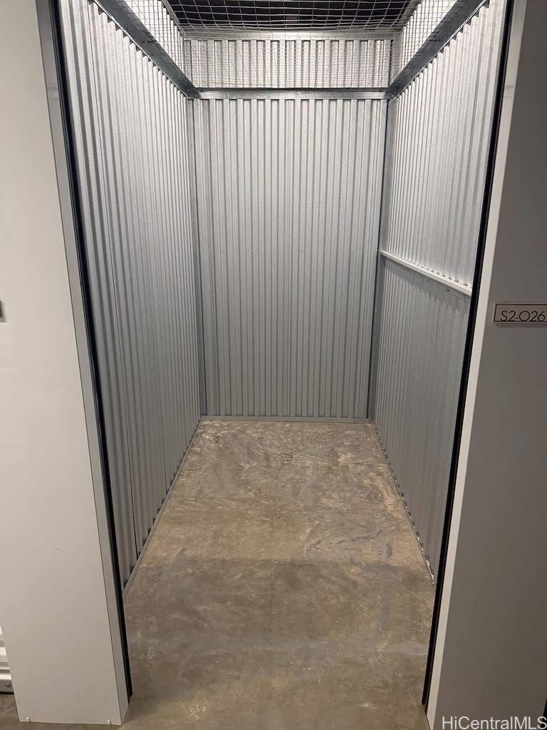 Empty metal storage unit with corrugated walls, mesh ceiling, and concrete floor.