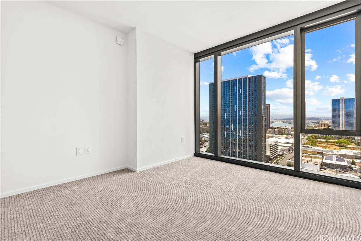 Empty carpeted room with floor-to-ceiling windows overlooking Honolulu’s city skyline.