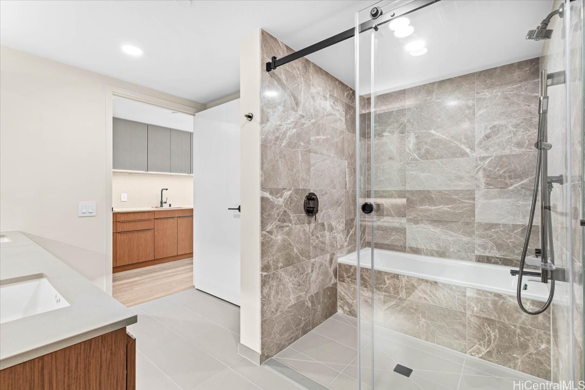 Bathroom with a glass-enclosed tub and shower, stone-look tile, and a wood vanity.