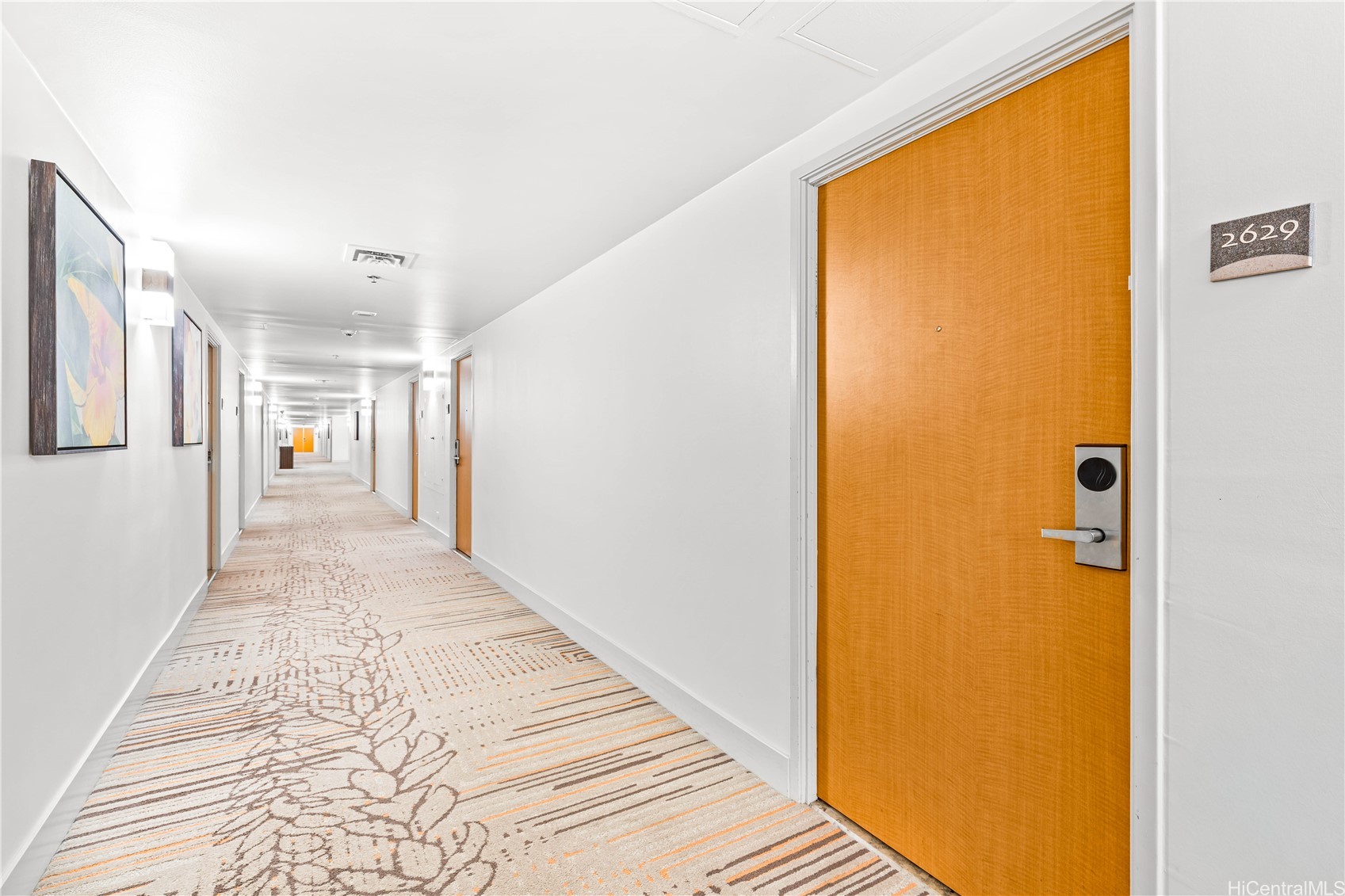 Condominium hallway with patterned carpet, framed artwork, and an orange door marked 2629.
