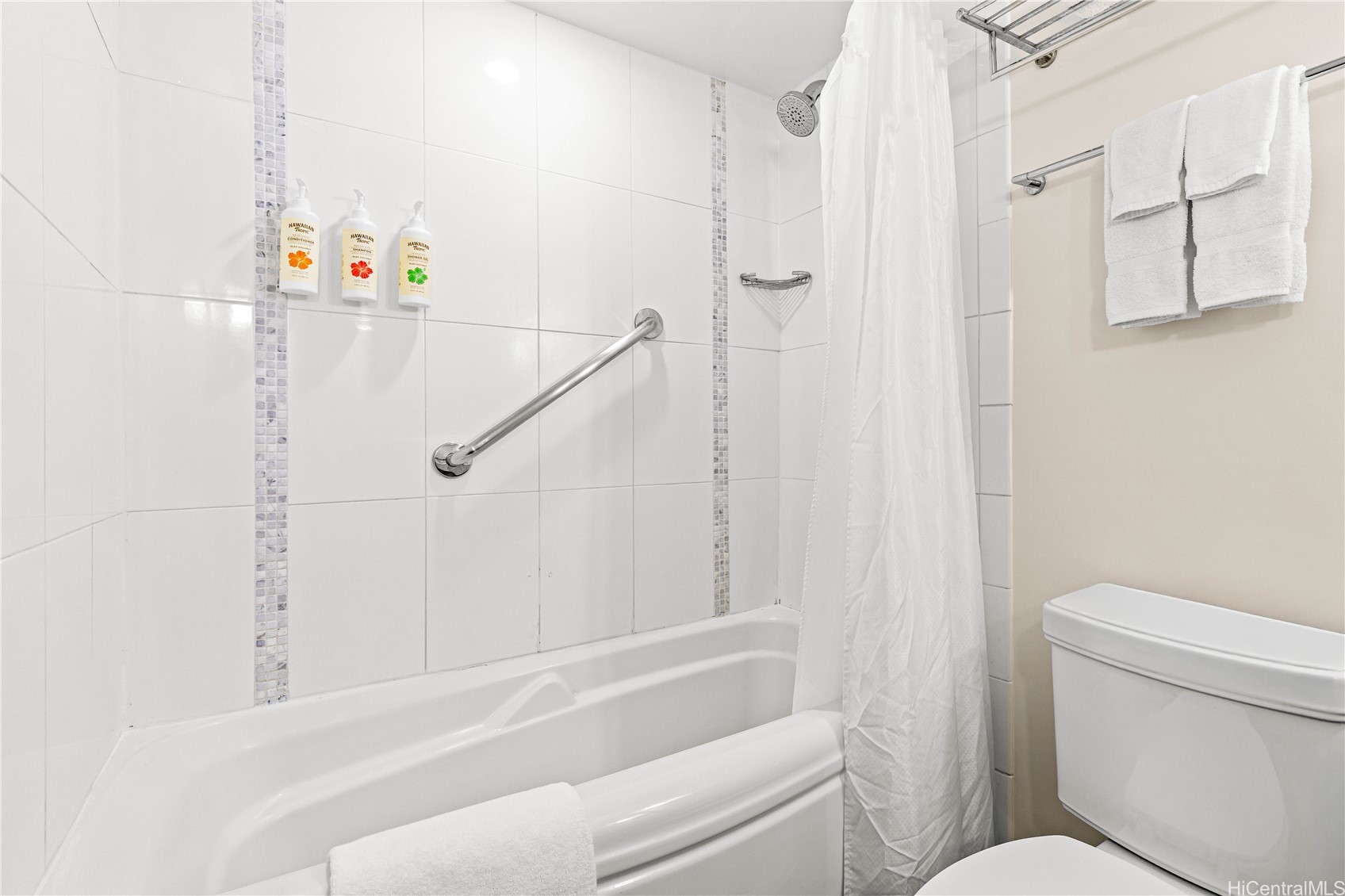 White-tiled bathroom with bathtub, shower curtain, chrome grab bar, and folded towels.