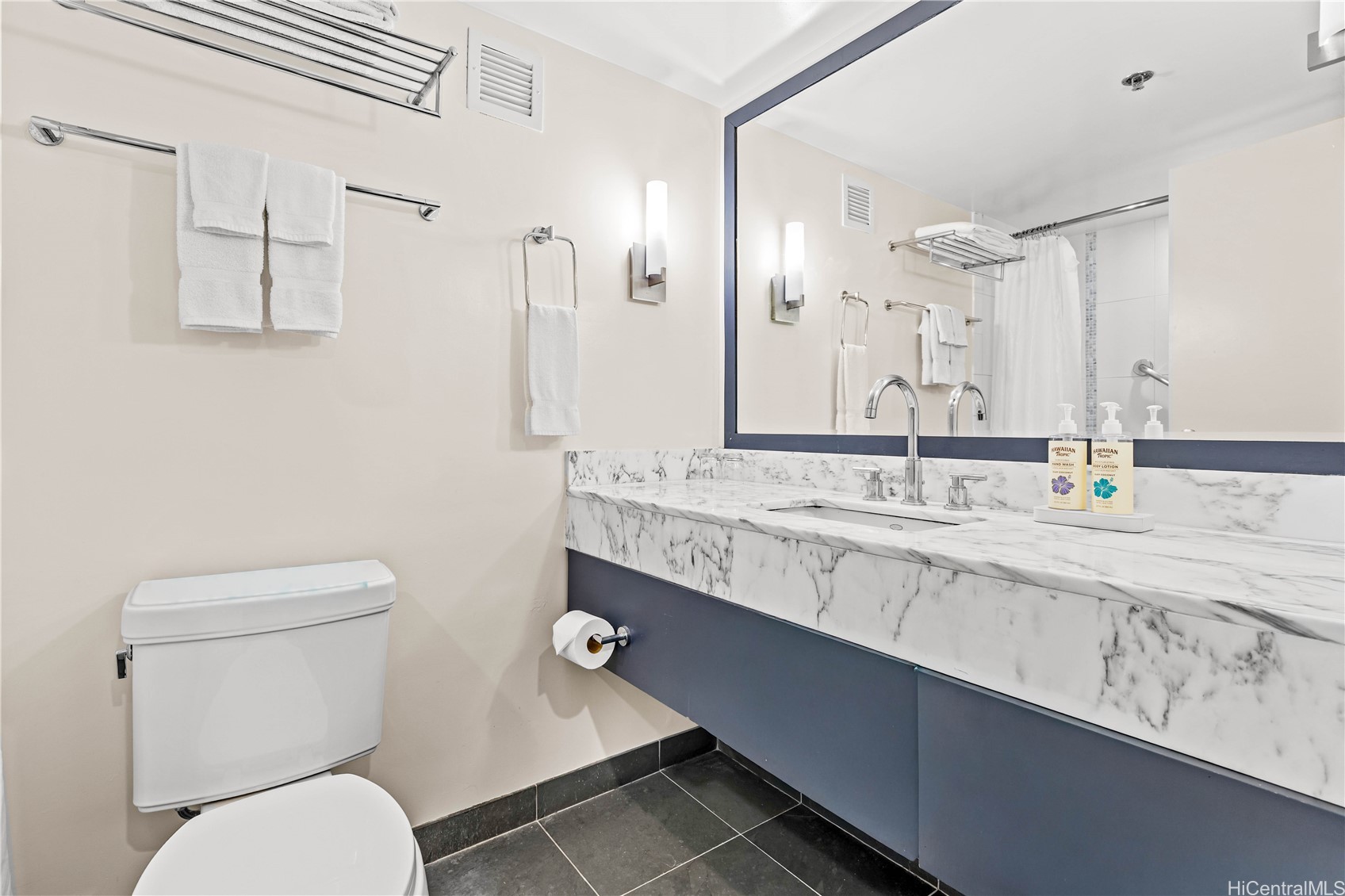 Bathroom with a marble-patterned vanity, large mirror, and shower reflected in the mirror.