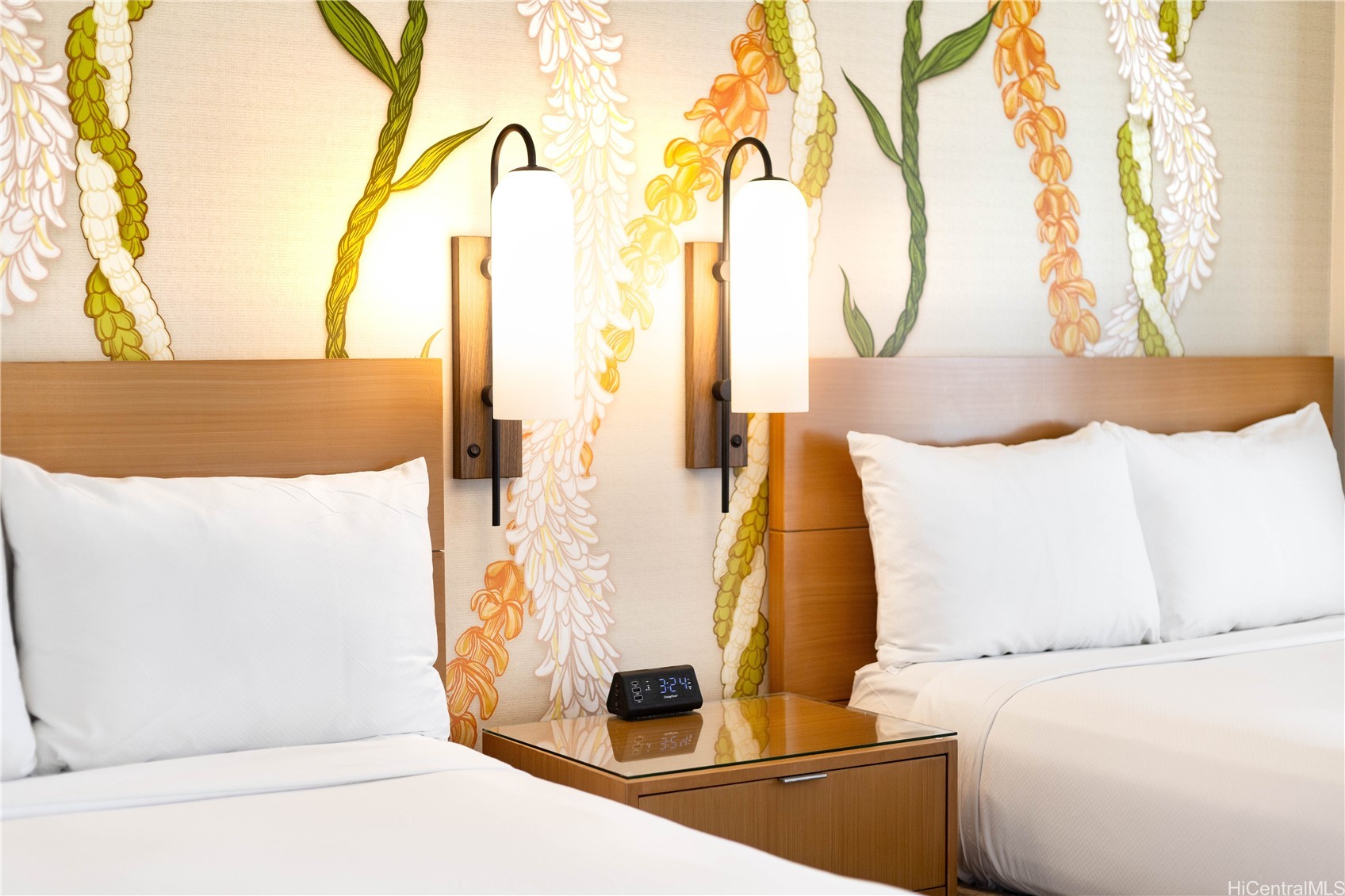 Bedroom with two white beds, floral wallpaper, warm wood headboards, and matching wall sconces.