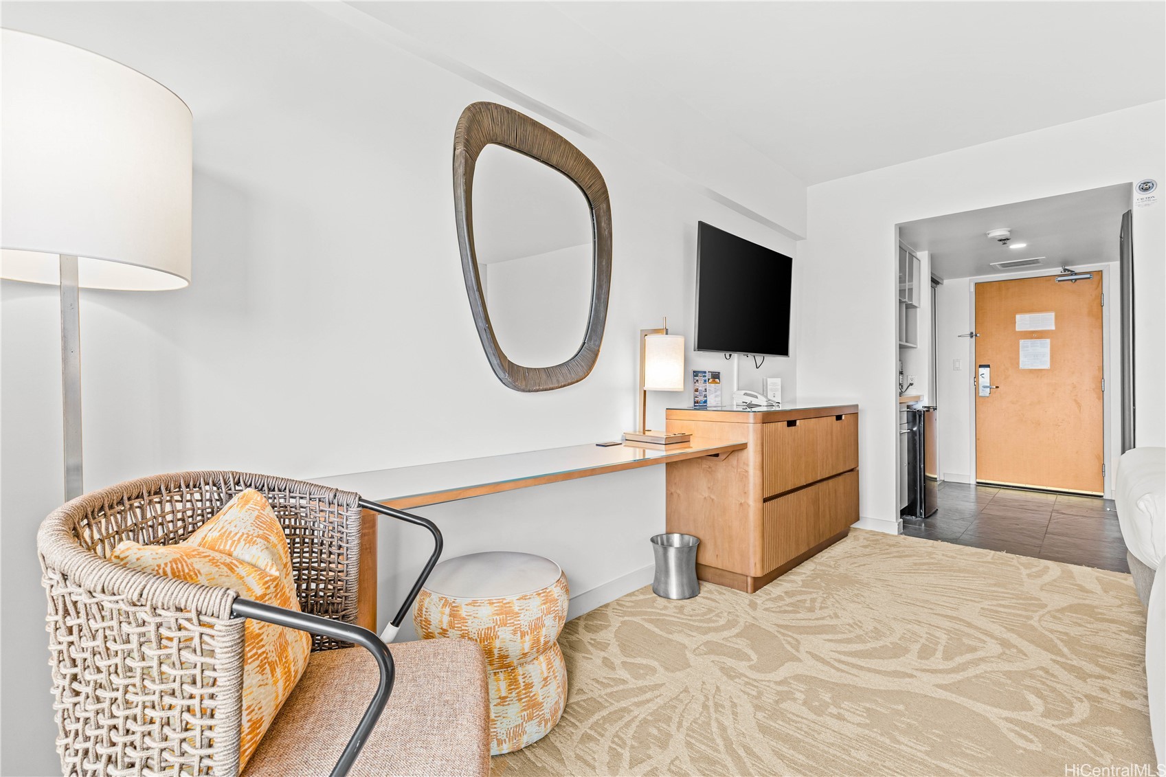 Furnished sitting area with a woven chair, wooden console, and wall-mounted television.