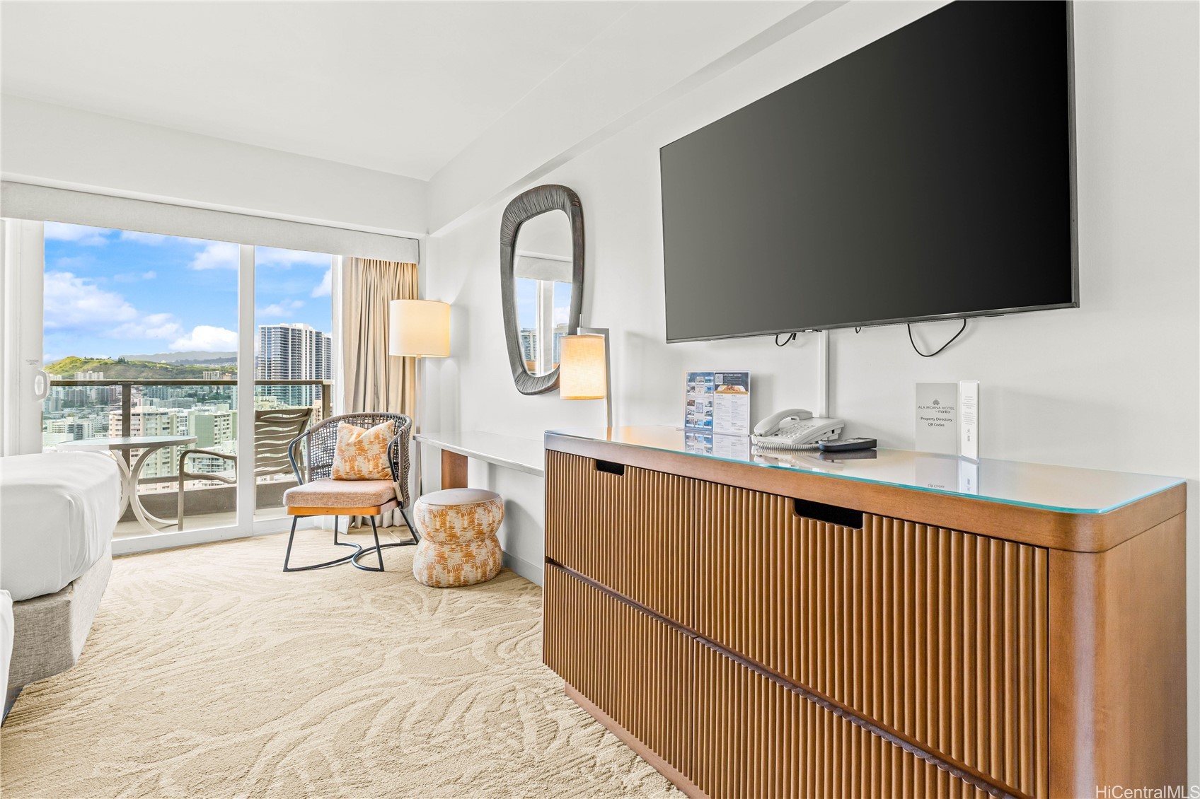 Furnished bedroom with a wall-mounted television and balcony overlooking the city.