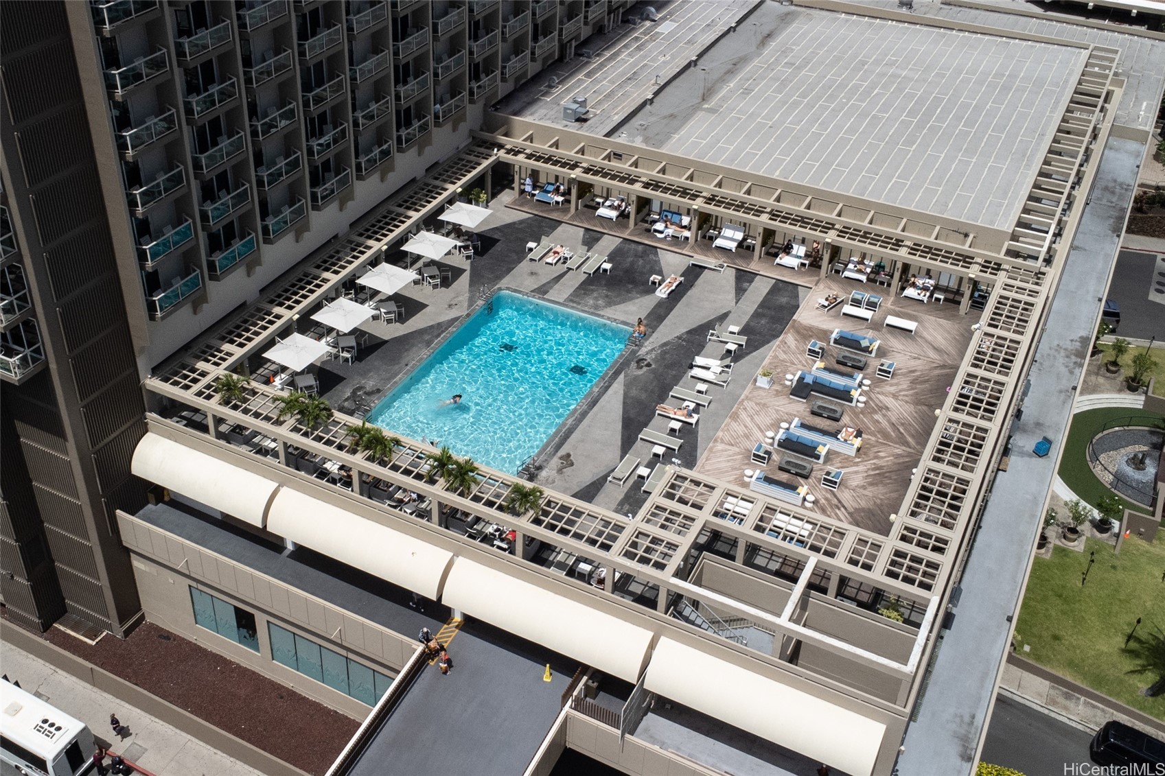 Aerial view of a rooftop pool deck with loungers, umbrellas, and outdoor seating.