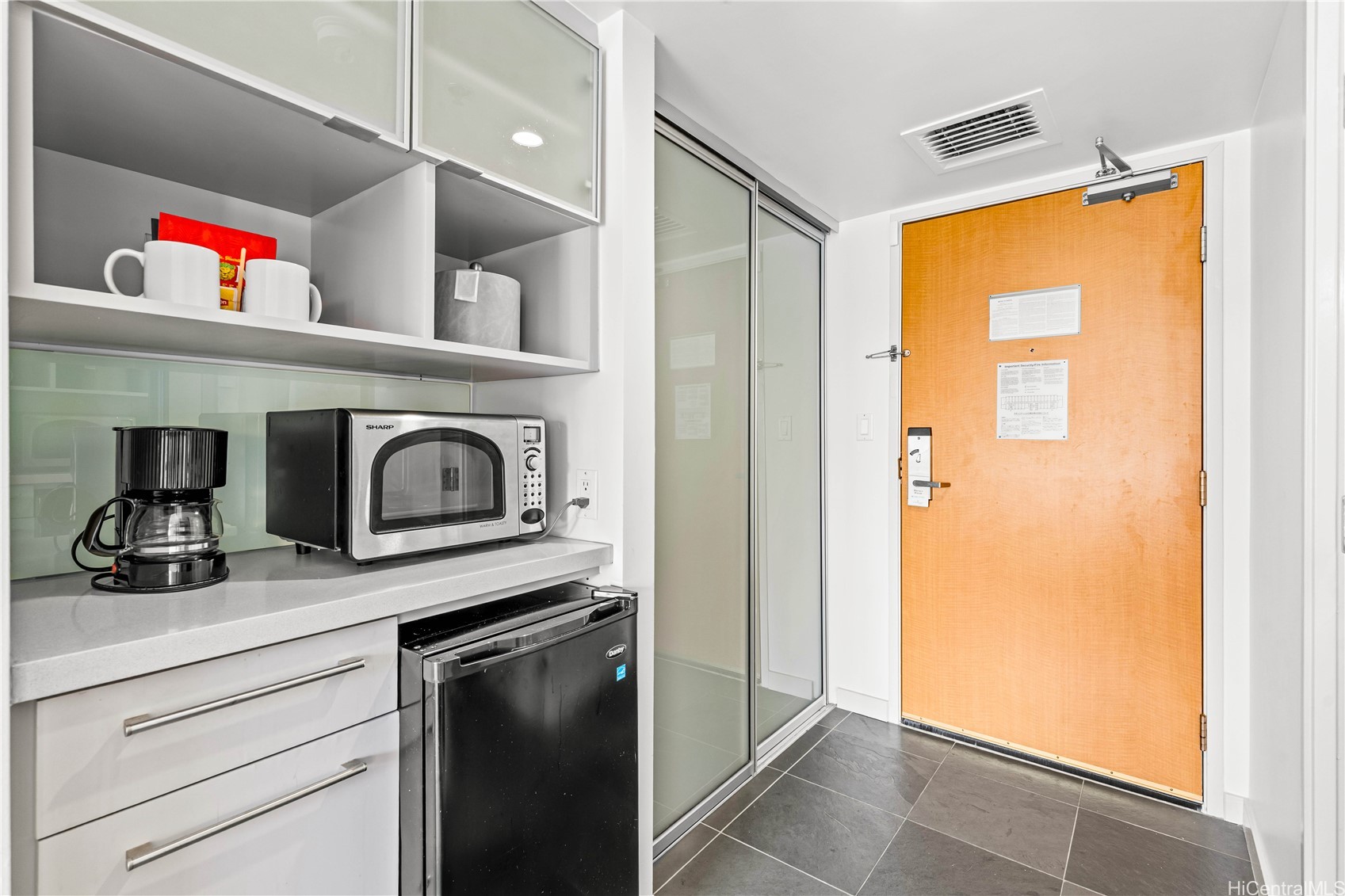 Compact condo kitchenette with a coffee maker, microwave, and mini-fridge beside the entry door.