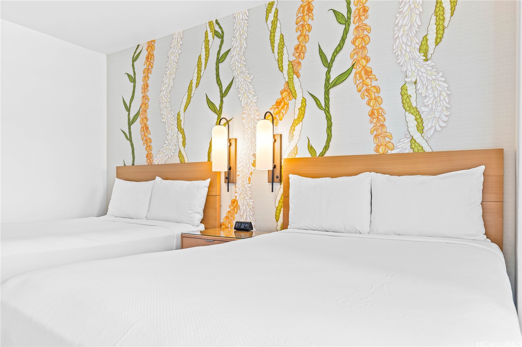 Bedroom with two white beds and a colorful lei mural behind the wooden headboard.