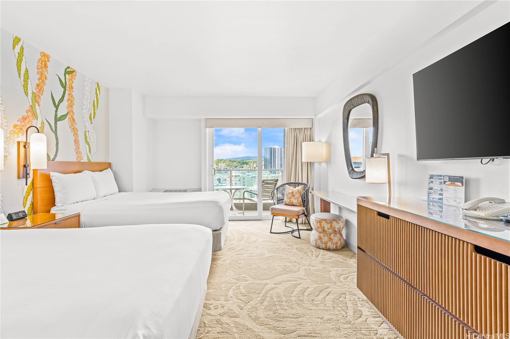 Furnished bedroom with two white beds, floral wall art, and balcony views of Honolulu.