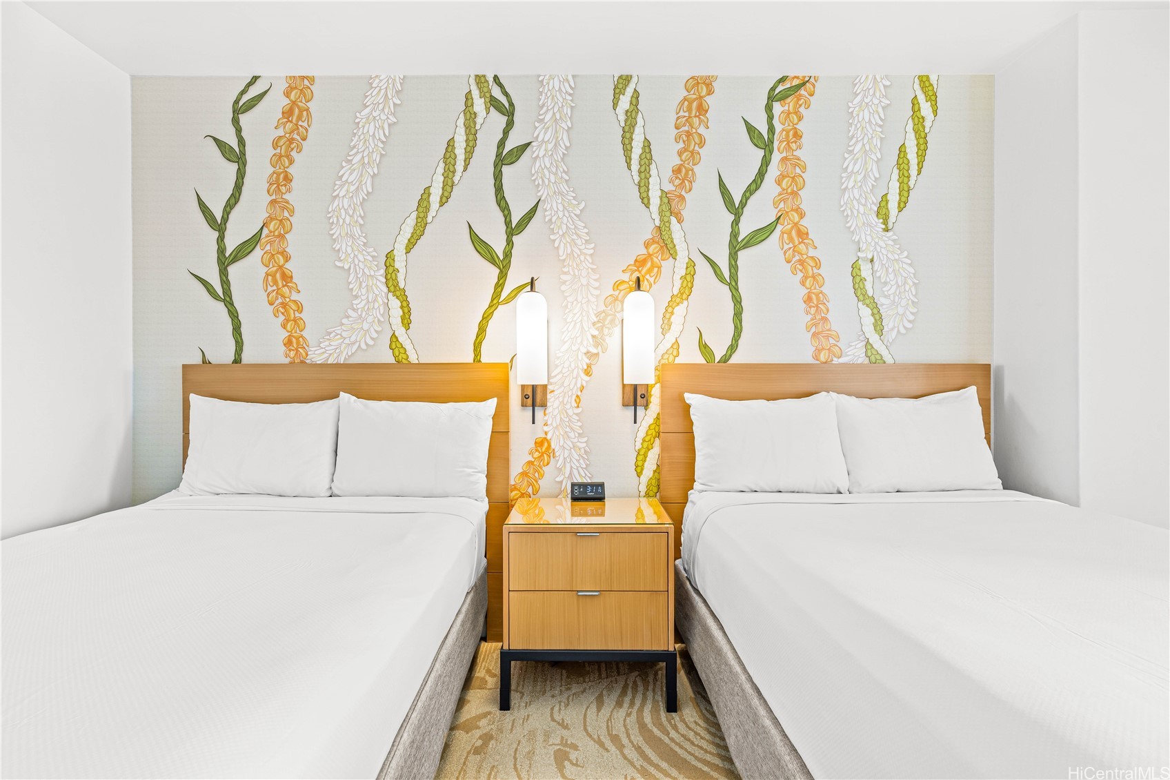 Bedroom with two white beds, floral lei-patterned wallpaper, and a shared nightstand.