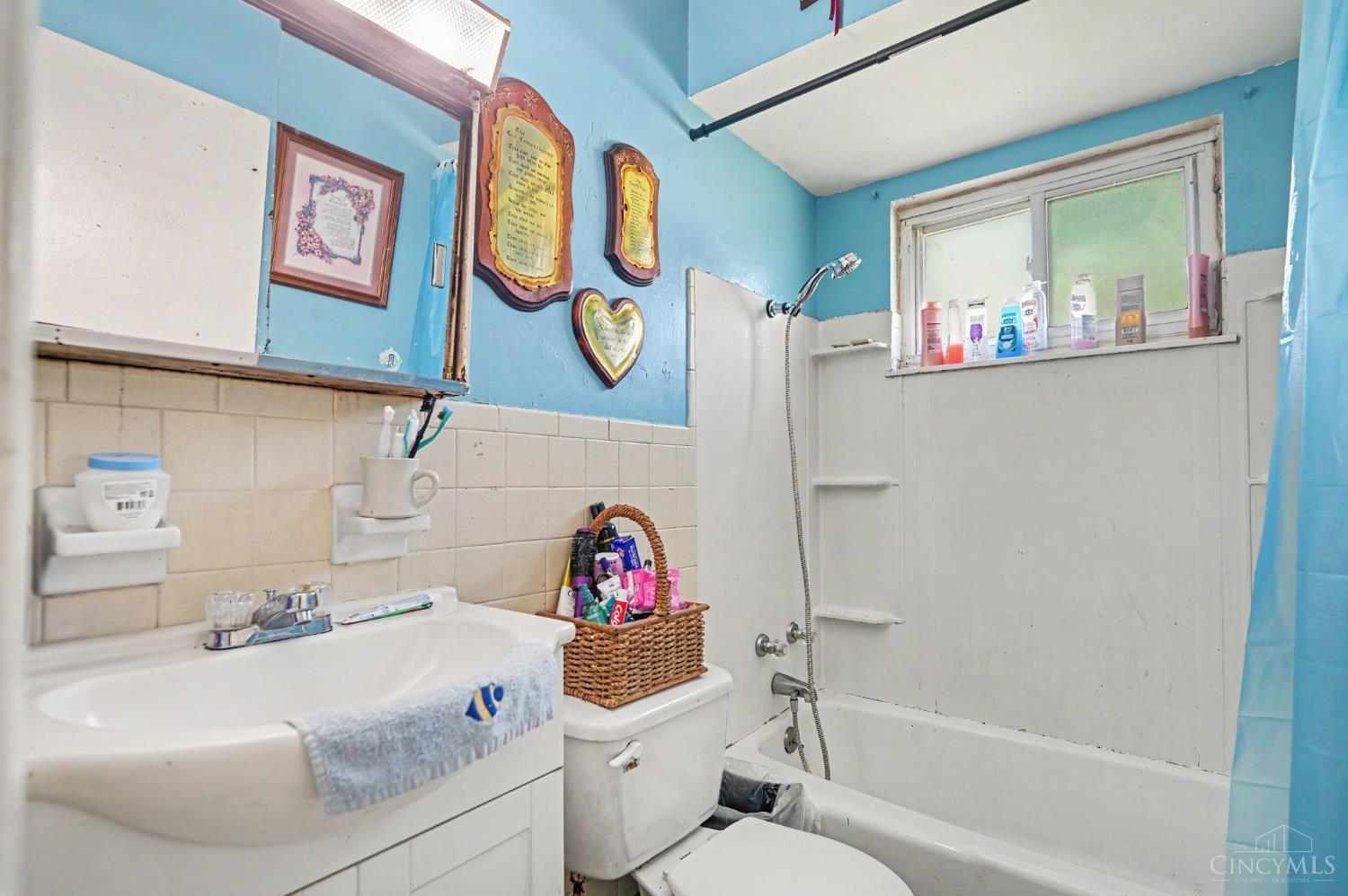 Bathroom with blue walls, cream tile, and a tub beneath a window.
