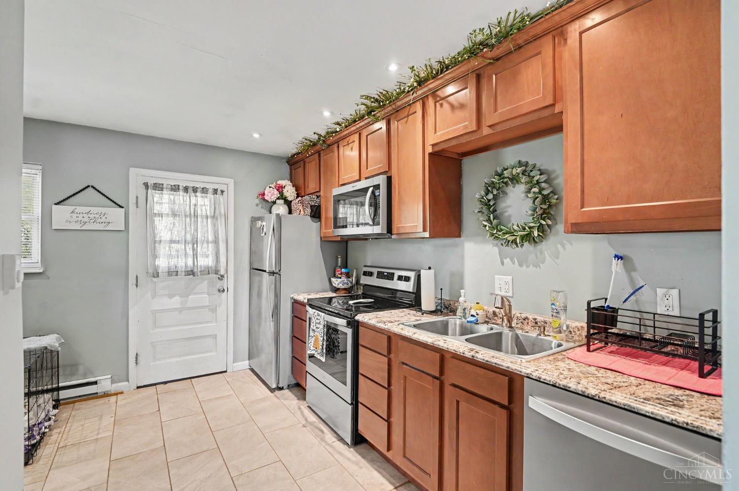 Kitchen with reddish-brown cabinets, speckled counters, stainless appliances, and a double sink.