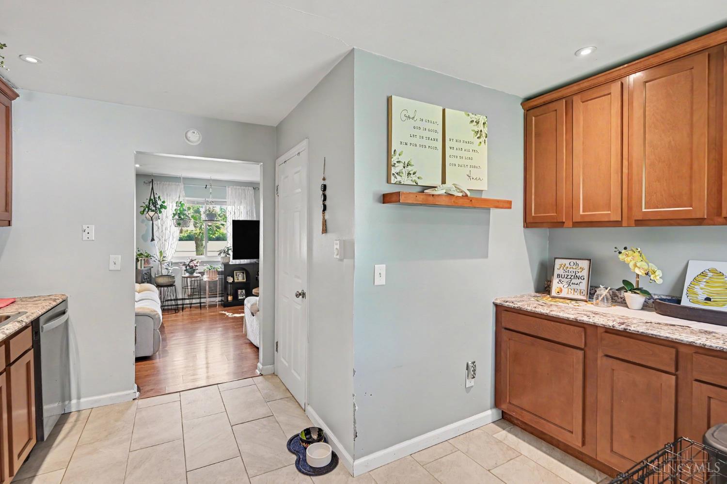 Kitchen with wooden cabinets and granite counters, opening into a plant-filled living room.