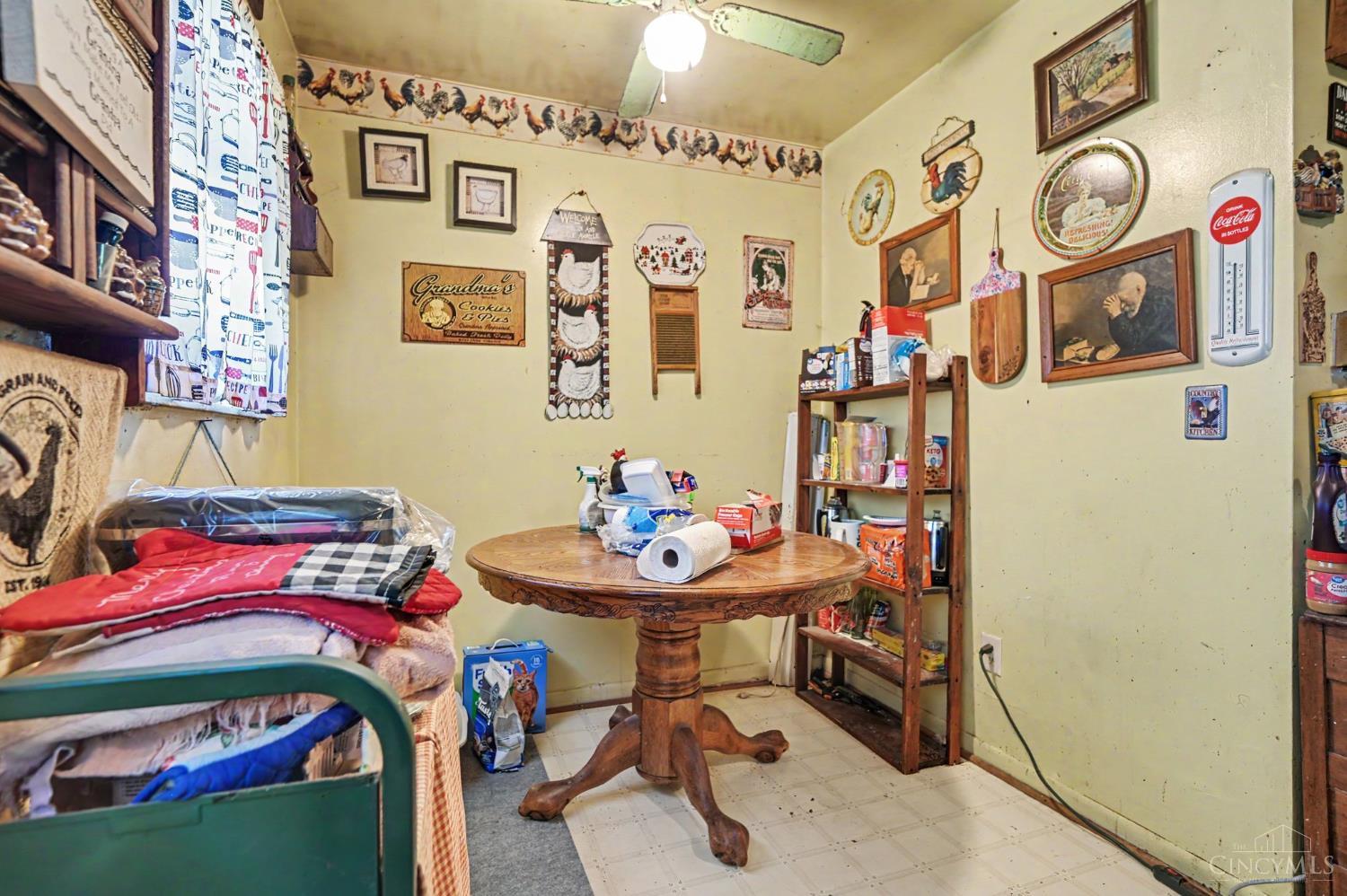 Cluttered kitchen with a round wooden table, open shelves, and rooster-themed decorations.