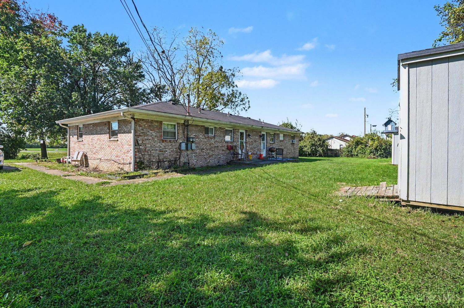 Single-story brick building beside a broad grassy yard, with trees and a detached outbuilding.