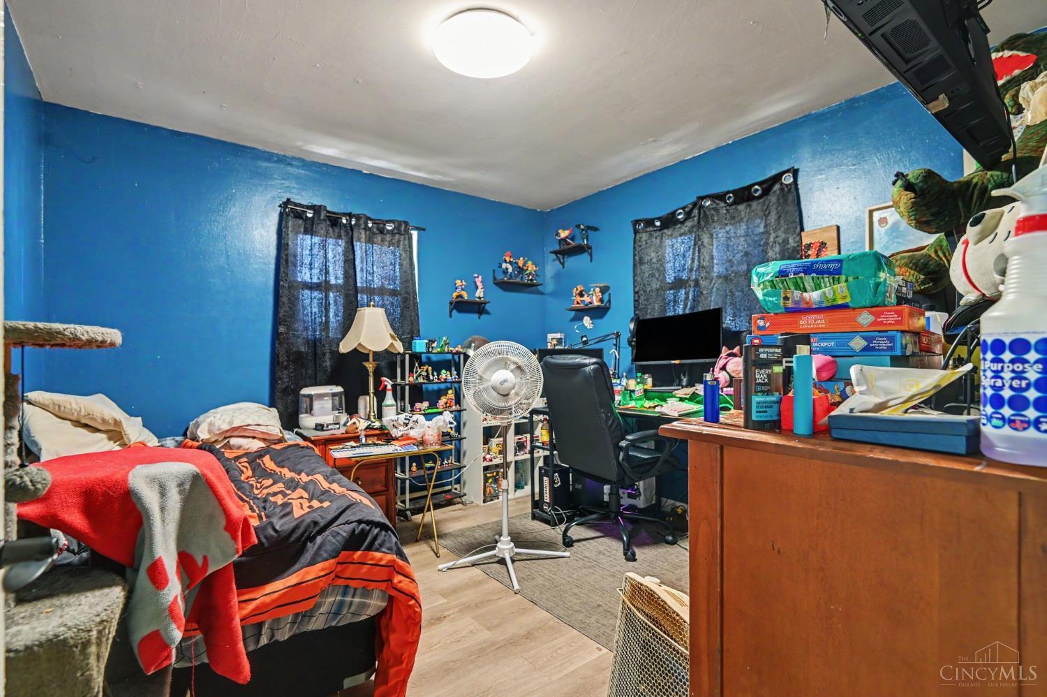 Crowded bedroom with bright blue walls, beds, and a desk with a computer.