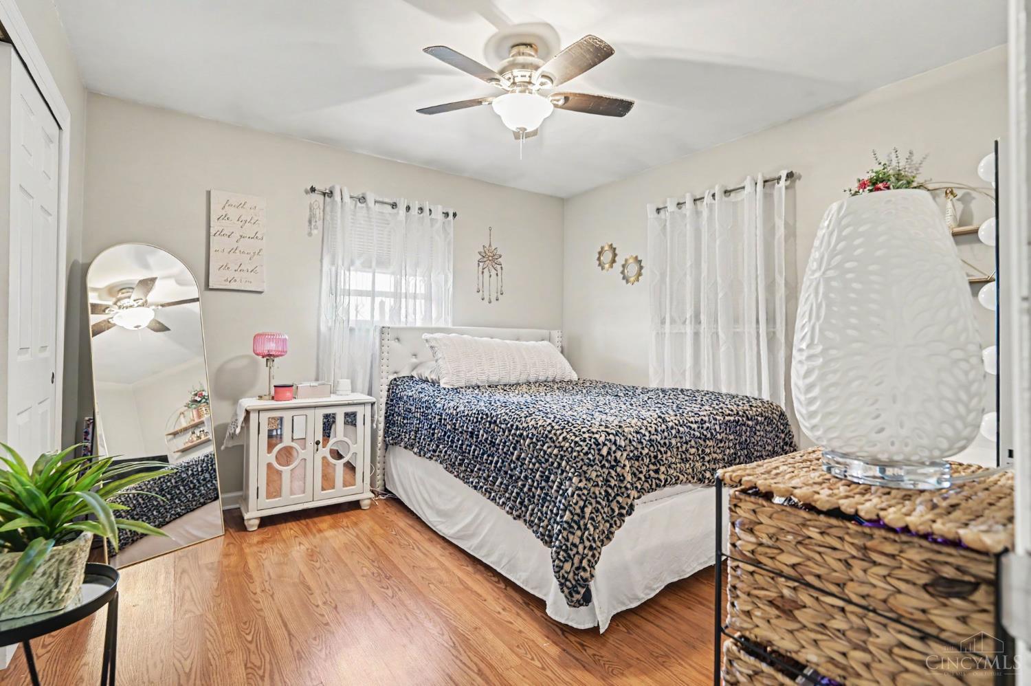 Furnished bedroom with a patterned bedspread, hardwood floors, and a ceiling fan.