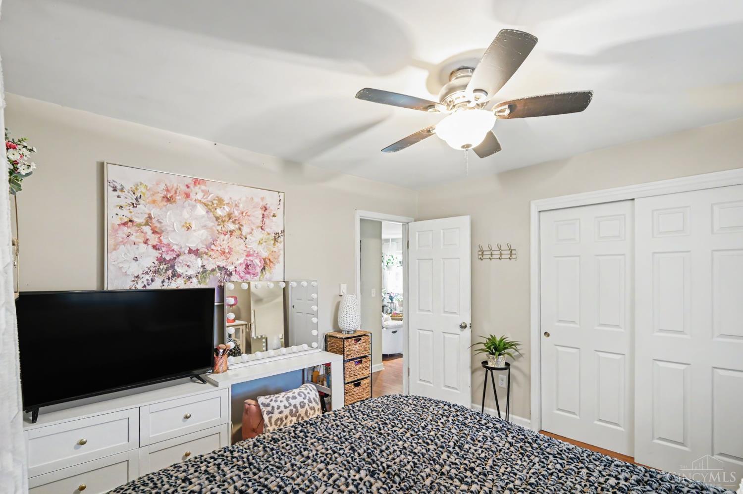 Bedroom with a patterned bed, ceiling fan, TV dresser, and floral wall art.