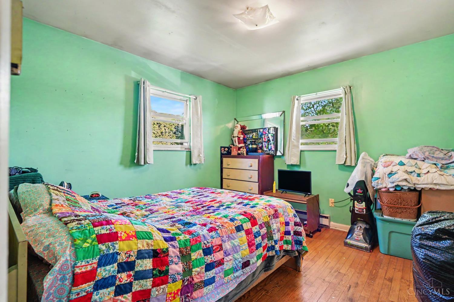Bedroom with mint-green walls, hardwood floors, and a colorful patchwork quilt on the bed.