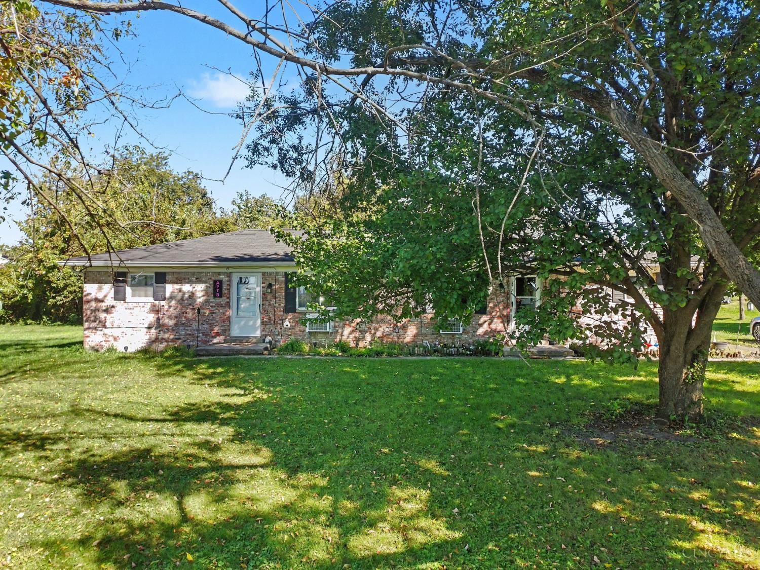 Single-story brick ranch house partly obscured by a large tree, with a broad front lawn.