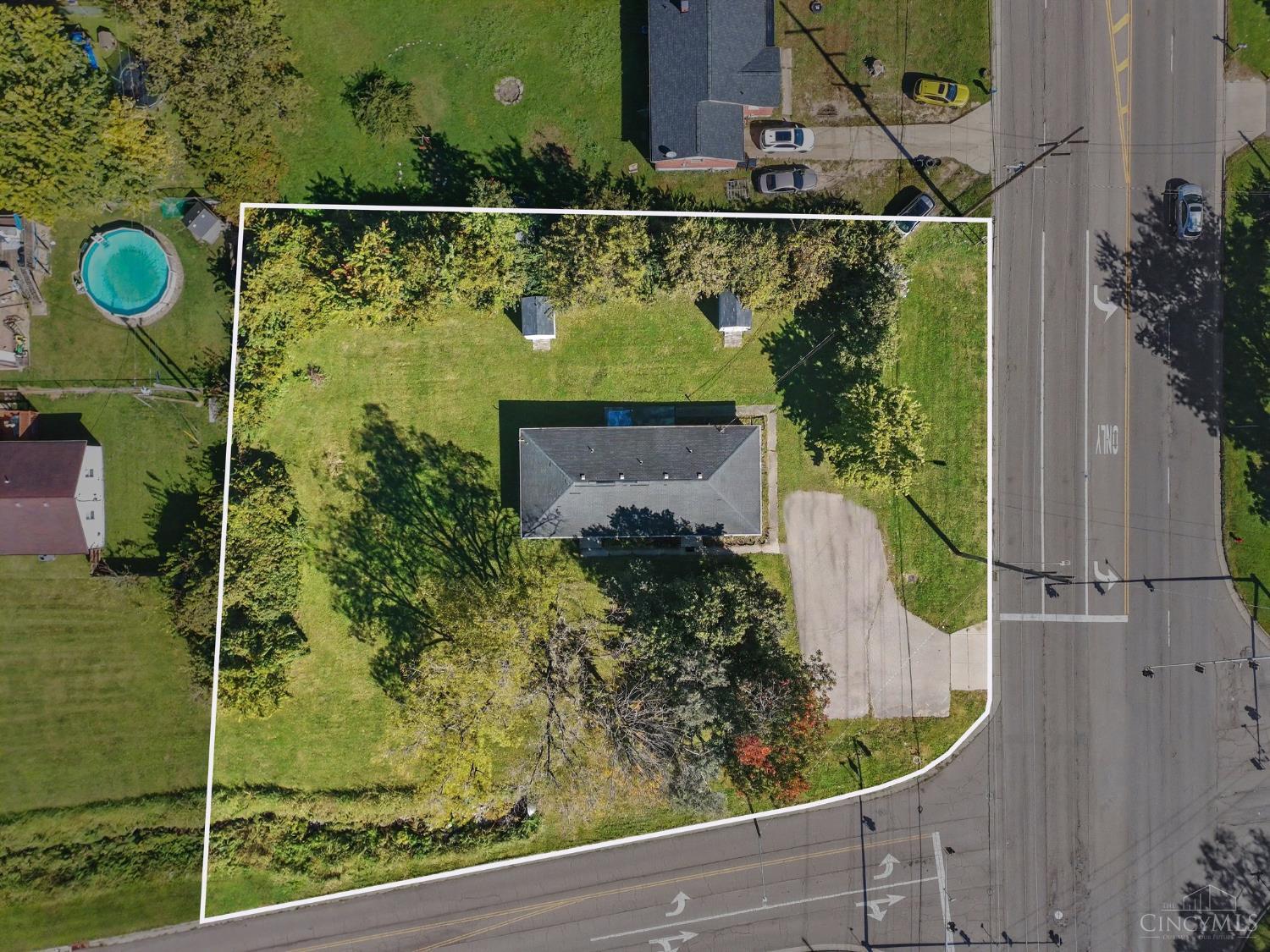 Aerial view of a corner lot outlined in white, with a house, lawn, mature trees and driveway.