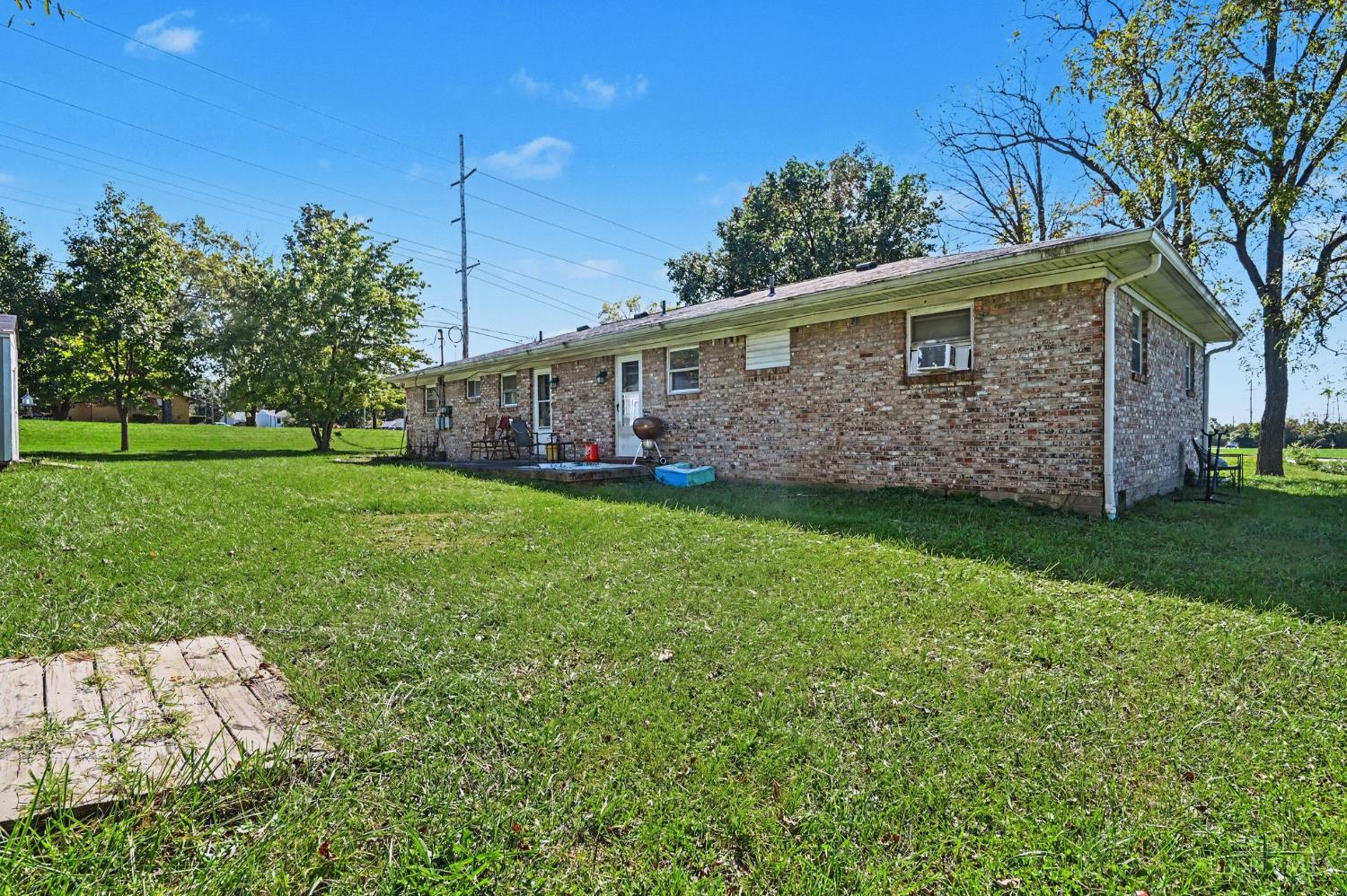 Rear of a single-story brick home beside a broad lawn, with a small patio and outdoor grill.