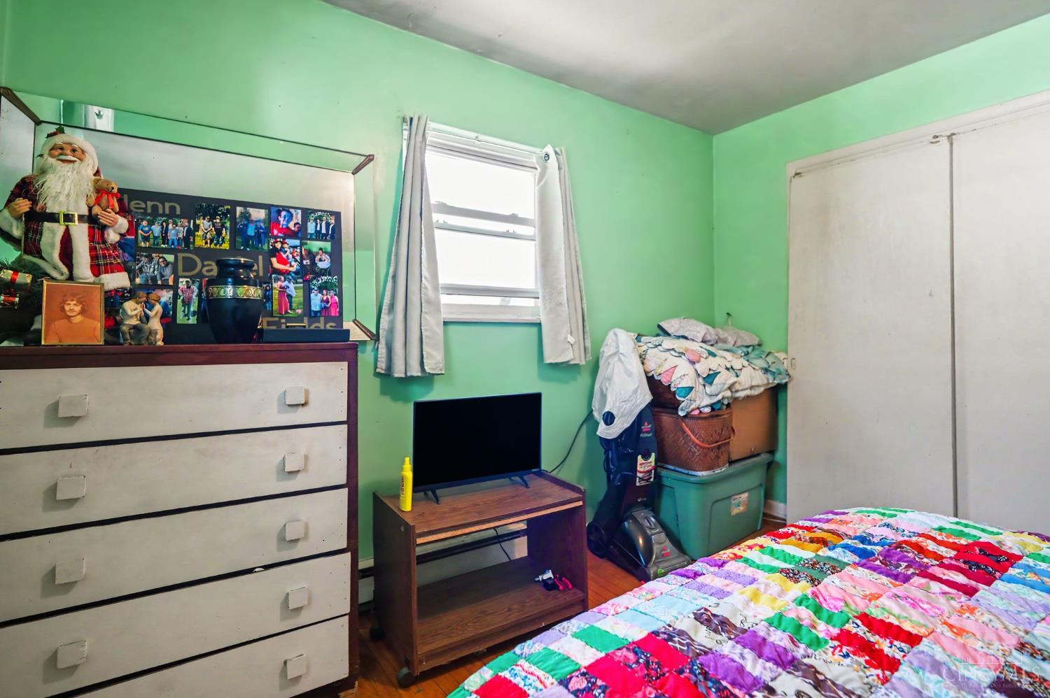 Bedroom with mint-green walls, a patchwork quilt, dresser, and television.