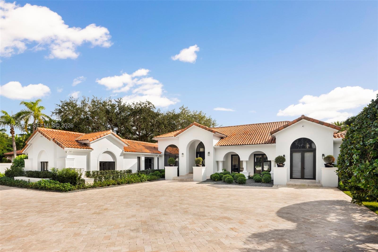 White stucco home with terracotta tile roofs, arched windows, and a broad paved driveway.