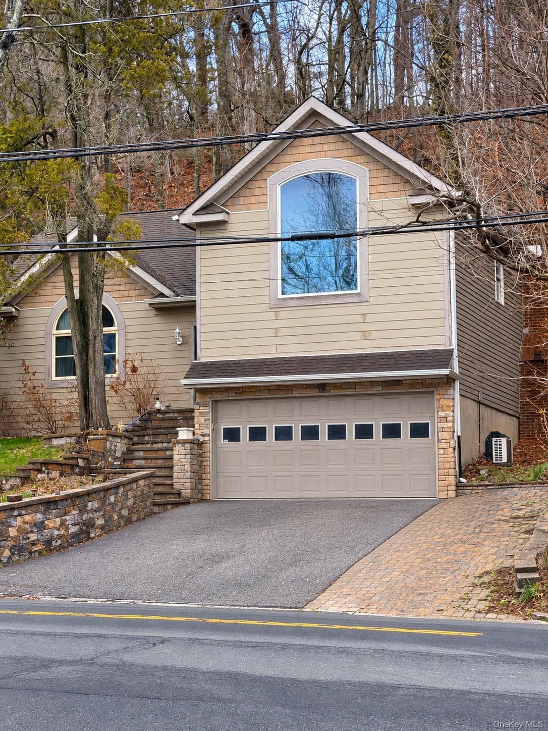 Tan-sided home with a large arched window, stone-accented garage, and wooded surroundings.